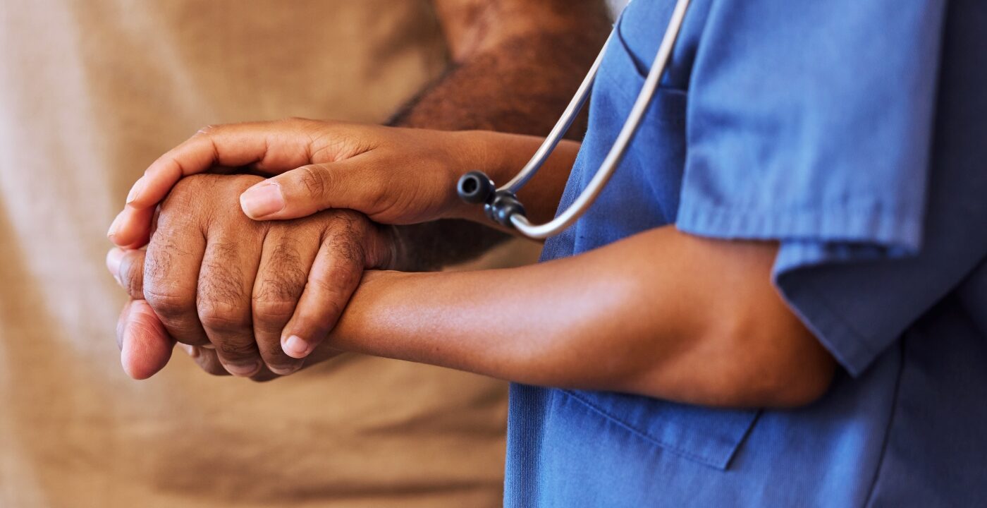 Health care provider in blue scrubs holding a patient’s hand