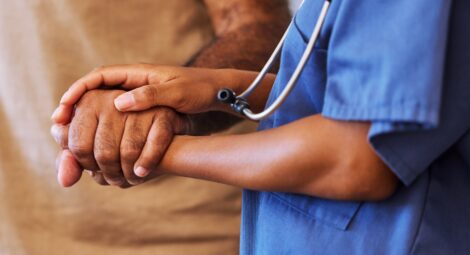 Health care provider in blue scrubs holding a patient’s hand