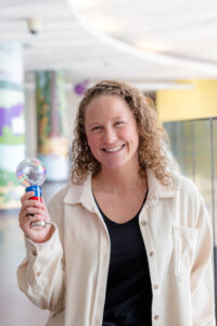 Woman with curly hair and white jacket smiles at camera and holds up a light wand
