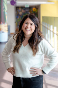 Woman with white sweater, hands on hips, smiles at camera