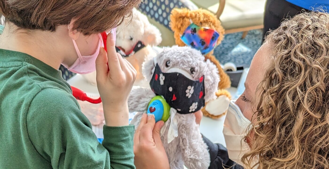Child life specialist demonstrates listening to the heart with a stethoscope on a stuffed toy for a child patient