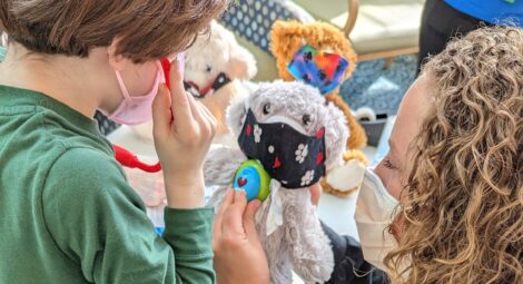 Child life specialist demonstrates listening to the heart with a stethoscope on a stuffed toy for a child patient