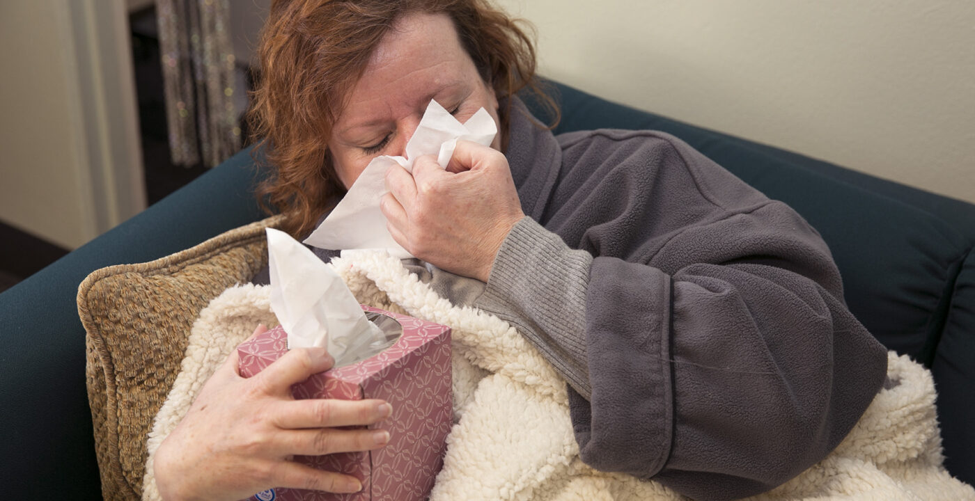 Woman blowing nose while sitting on couch