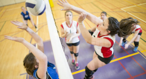 During a teenage girl volleyball match one team has just spiked the ball, the ball crossed the net and now the opposing team is trying to block it.