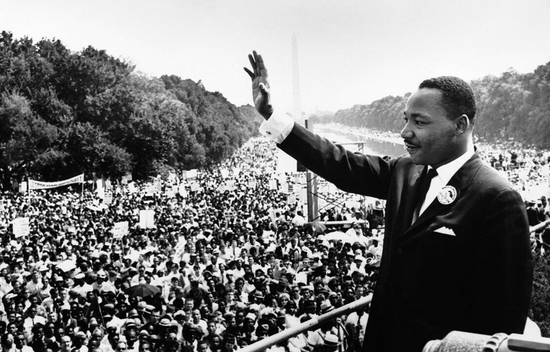 Martin Luther King Jr. waves at a large crowd from a stage