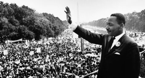 Martin Luther King Jr. waves at a large crowd from a stage
