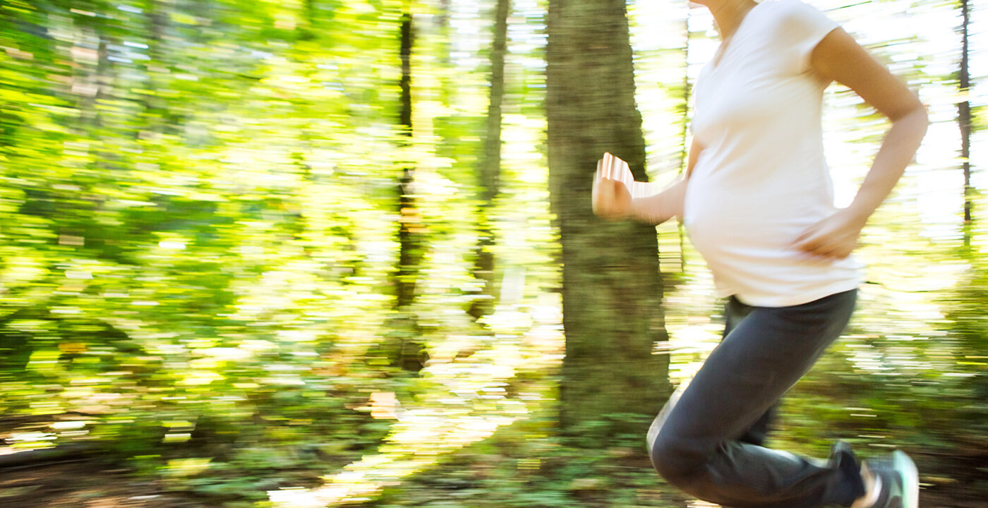 Pregnant woman running throuh the woods.
