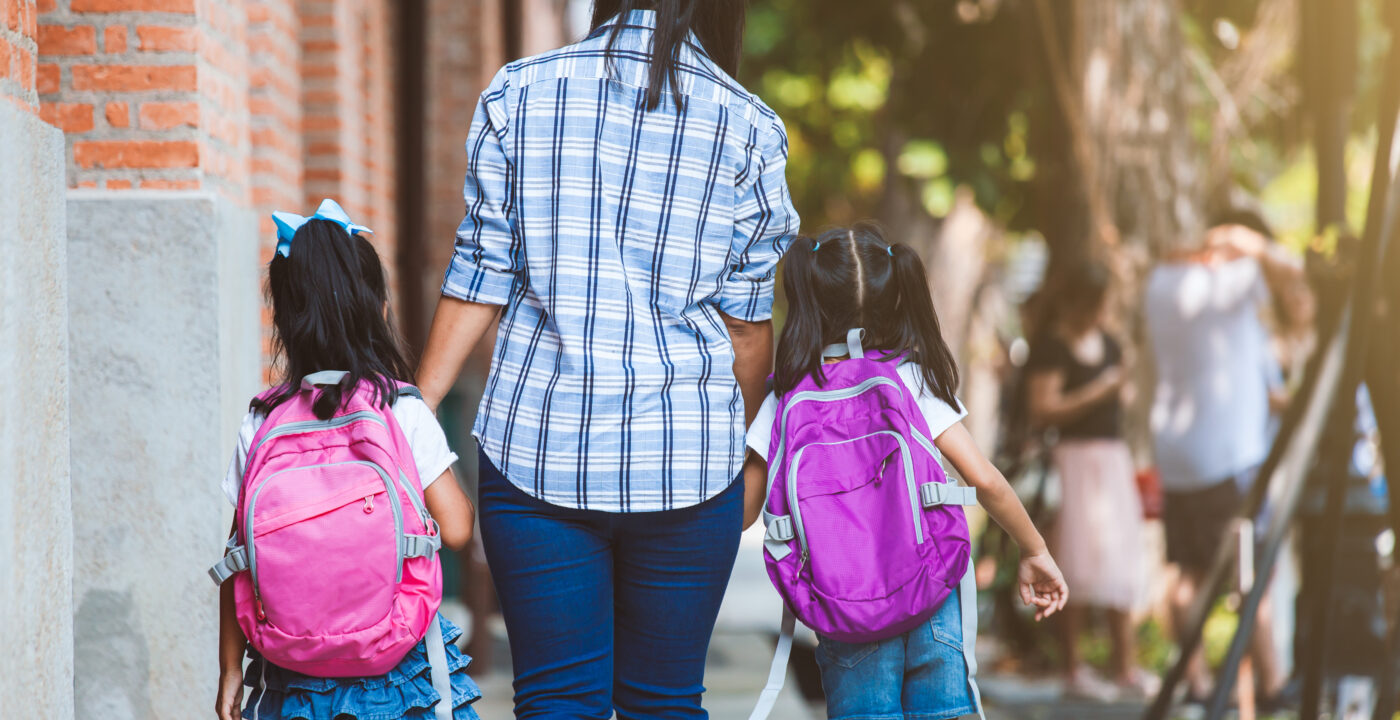 Two kids with backpacks walking with an adult