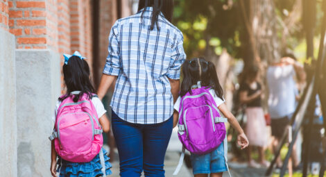 Two kids with backpacks walking with an adult