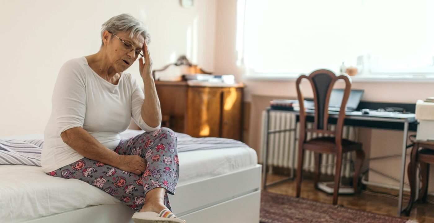 Woman sitting on bed grabbing her head