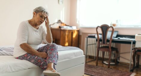 Woman sitting on bed grabbing her head