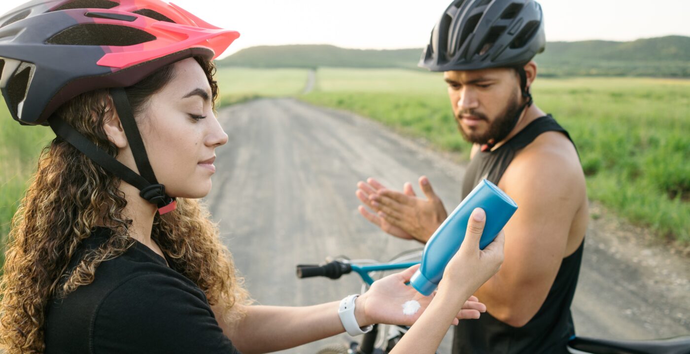 Two people on bicycles breaking to apply sunscreen.