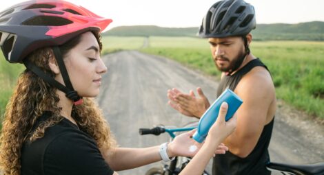 Two people on bicycles breaking to apply sunscreen.