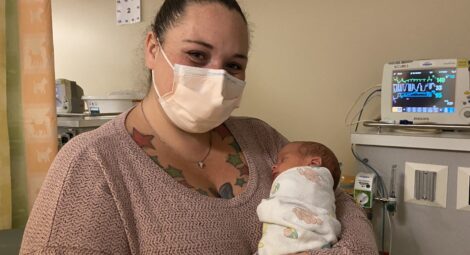 Woman in sweater holds swaddled infant in hospital room