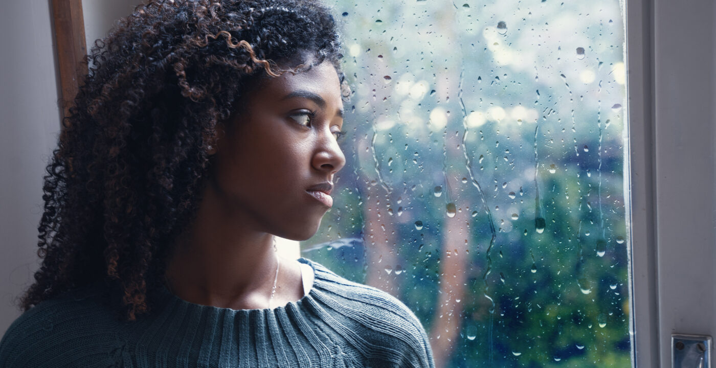 Woman sadly looks out a rain-soaked window