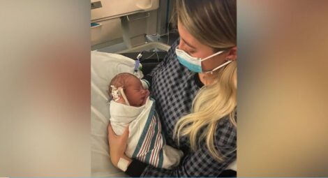 Blonde woman holds premature infant in hospital room.