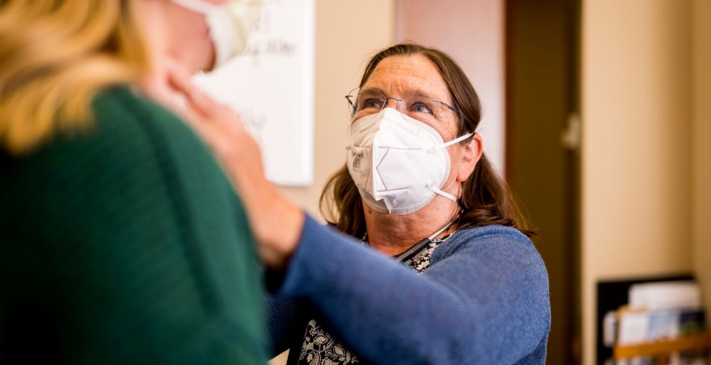 Woman doctor wearing face mask examines blonde patient’s lymph nodes