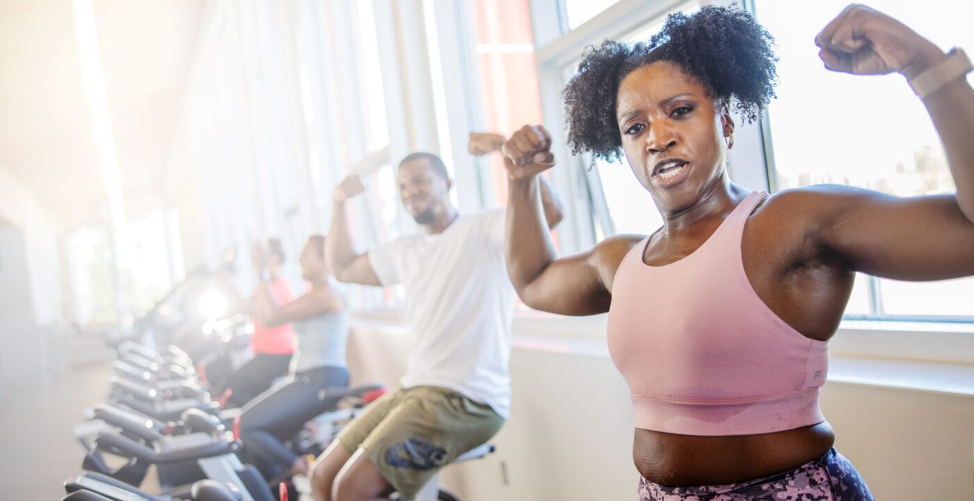 Woman on an exercise bicycle flexing her biceps