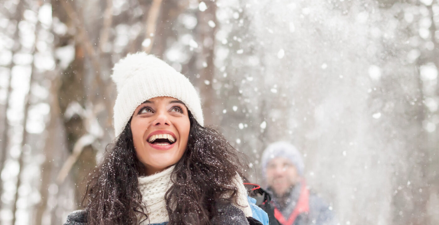 Woman wearing winter hat, scarf and gloves looks up in wonder as it snows around her