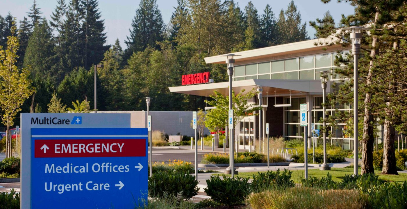 Exterior view of a MultiCare emergency department sign with arrows pointing toward the emergency department building behind it