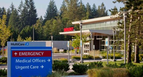 Exterior view of a MultiCare emergency department sign with arrows pointing toward the emergency department building behind it