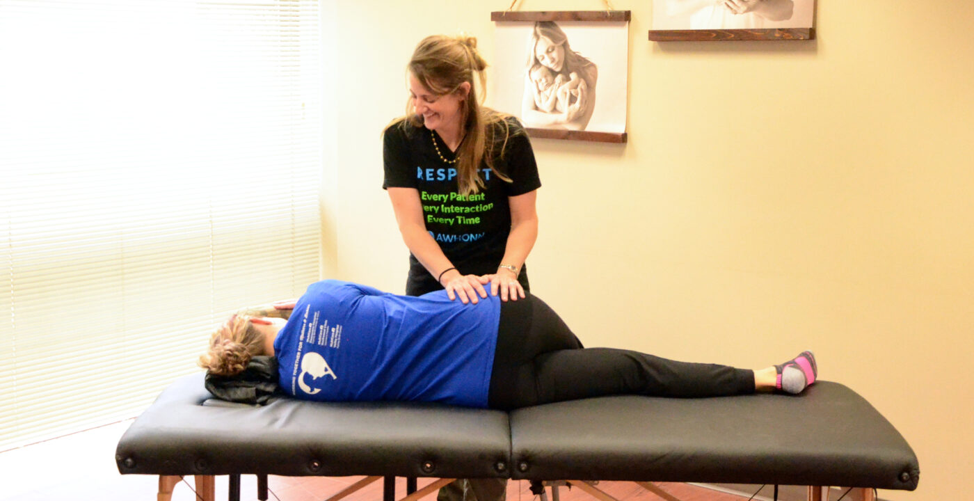 Woman instructs another woman lying on massage table through an exercise