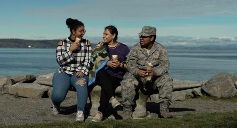 Three people sitting on a bench in front of the Puget Sound on a sunny day