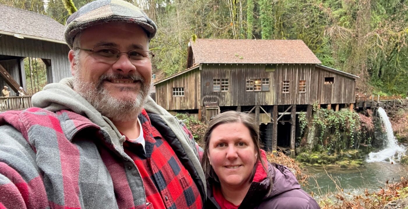 Couple standing in front of river with old wooden building in background