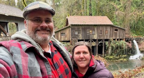 Couple standing in front of river with old wooden building in background