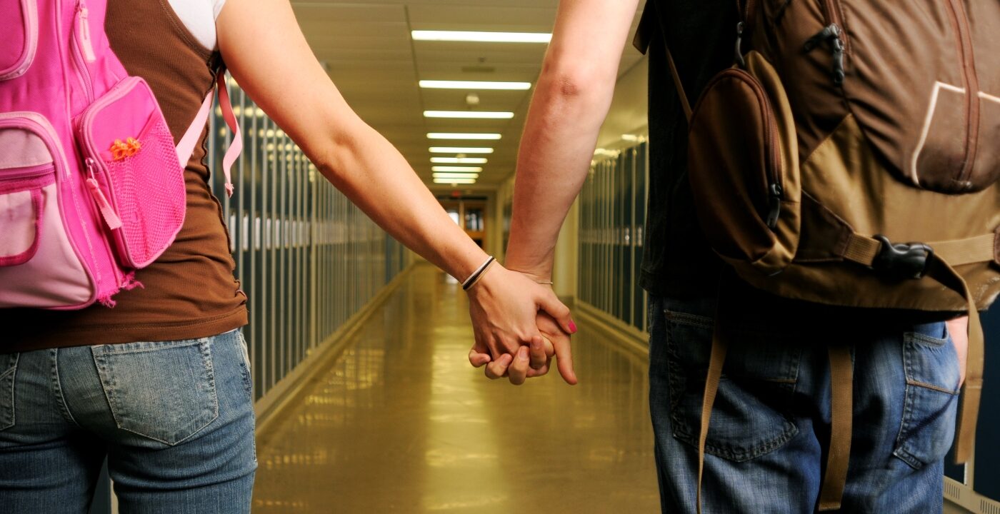 Teenage-appearing individuals wearing backpacks and holding hands