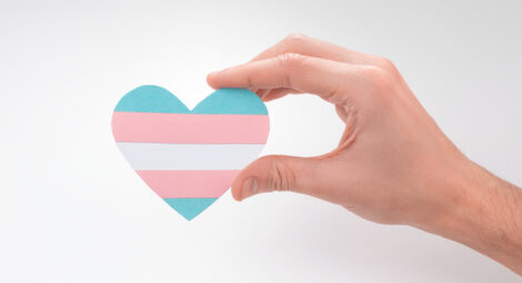 A person’s hand holds a paper heart with the transgender pride colors