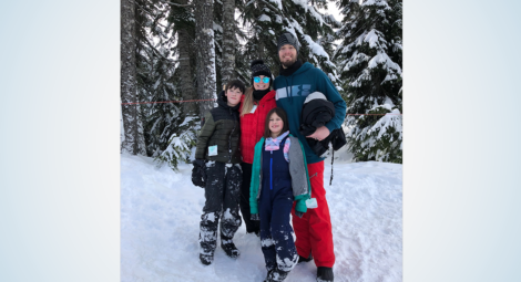 Mom, dad, son and daughter pose in snow gear in a wooded setting