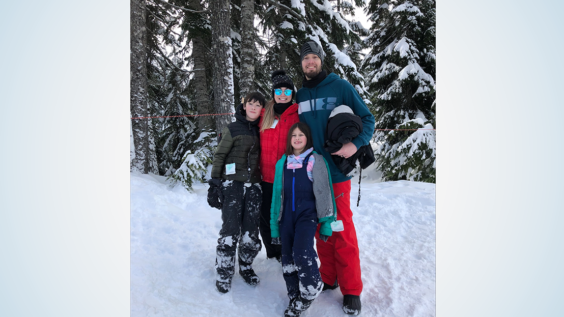 Mom, dad, son and daughter pose in snow gear in a wooded setting