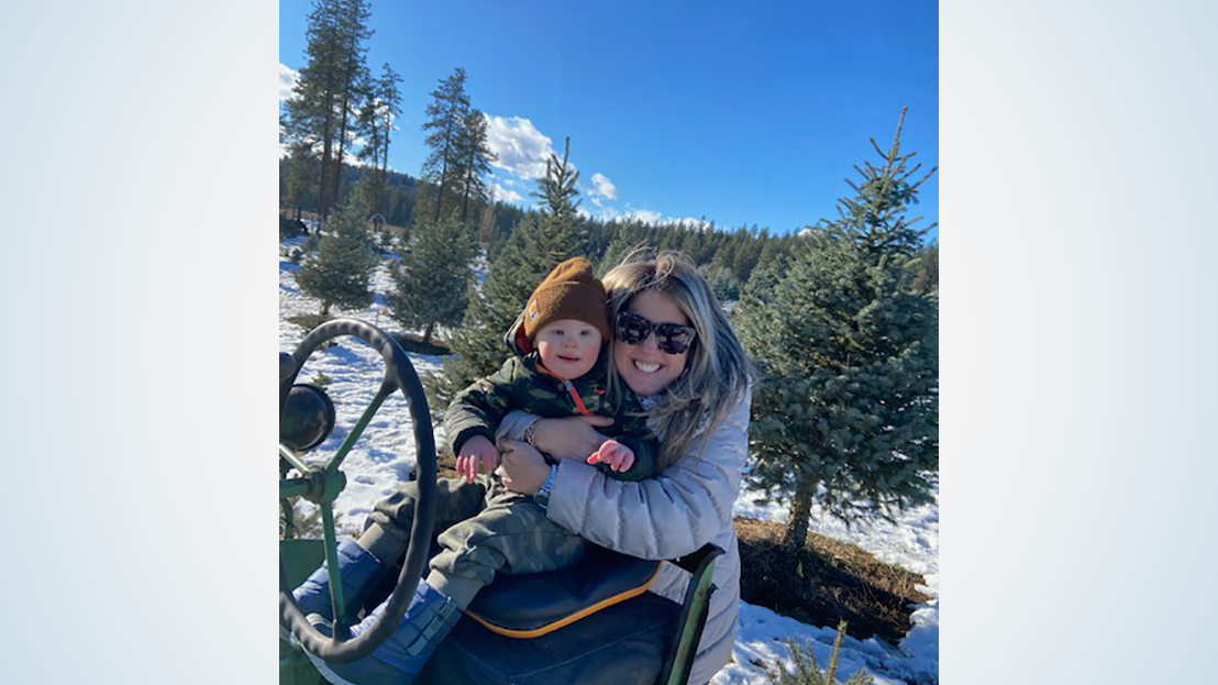 Mom and toddler smile at camera in a sunny woodsy scene