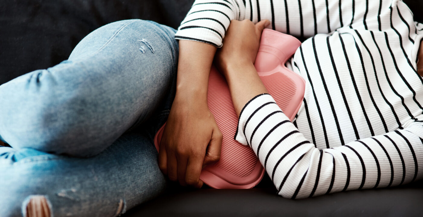 Woman holding hot water bottle against abdomen