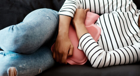 Woman holding hot water bottle against abdomen