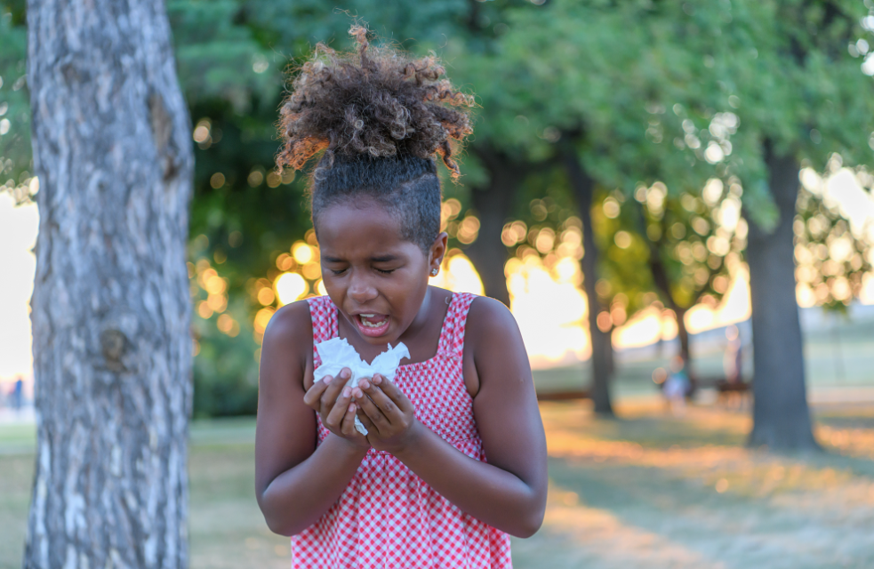 Young girl sneezing into a tissue due to seasonal allergies