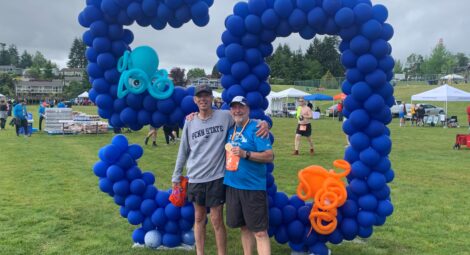 Two man stand side by side in front a “50” balloon decoration in a park