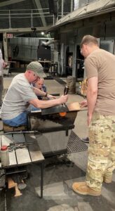 A team of veterans and active-duty military shape a ball of hot glass into a drinking glass