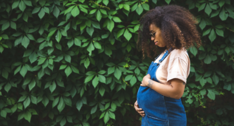 Side view of woman holding pregnant stomach against a wall of leaves