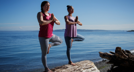 Two women doing yoga on a log by the water