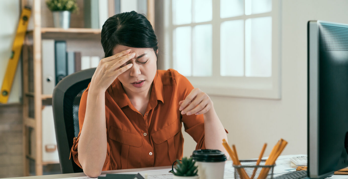 Woman sitting at desk holding head in pain