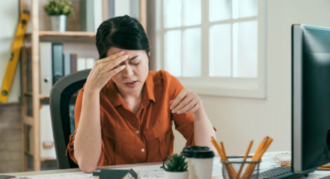 Woman sitting at desk holding head in pain