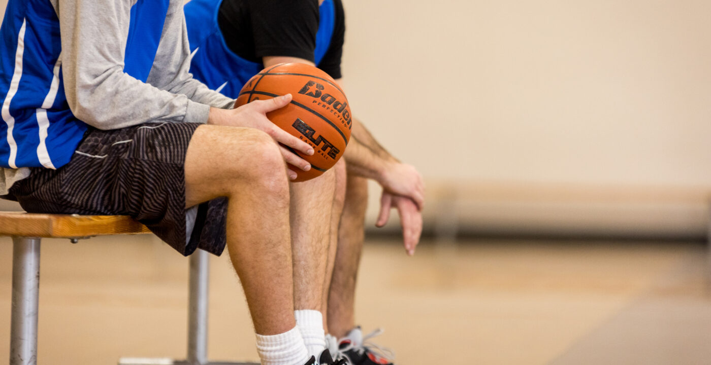 Basketball players sit on bench at basketball court, one holding a basketball