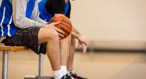 Basketball players sit on bench at basketball court, one holding a basketball