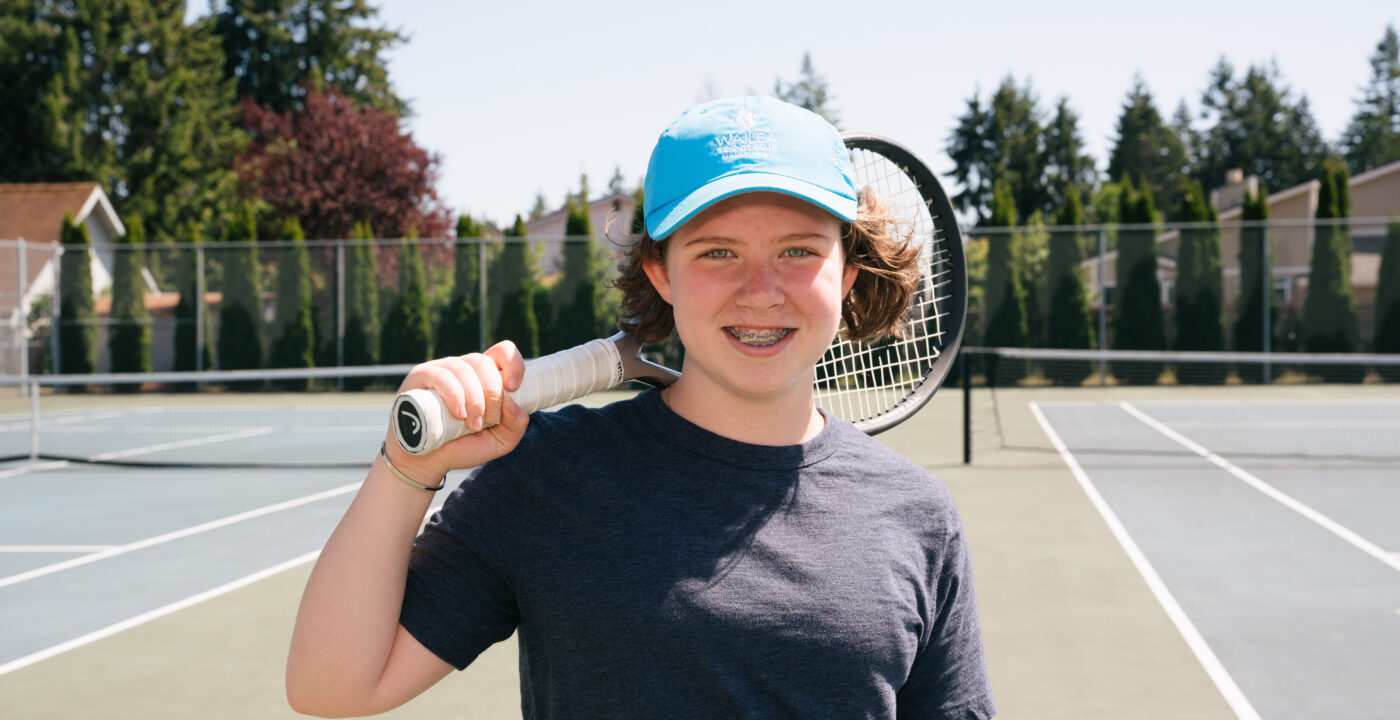 Teen boy in baseball cap poses on tennis court holding a racket