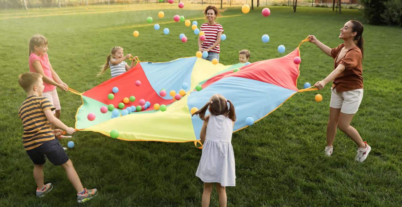 Students and adult playing game with parachute in grassy field
