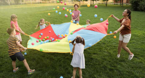 Students and adult playing game with parachute in grassy field