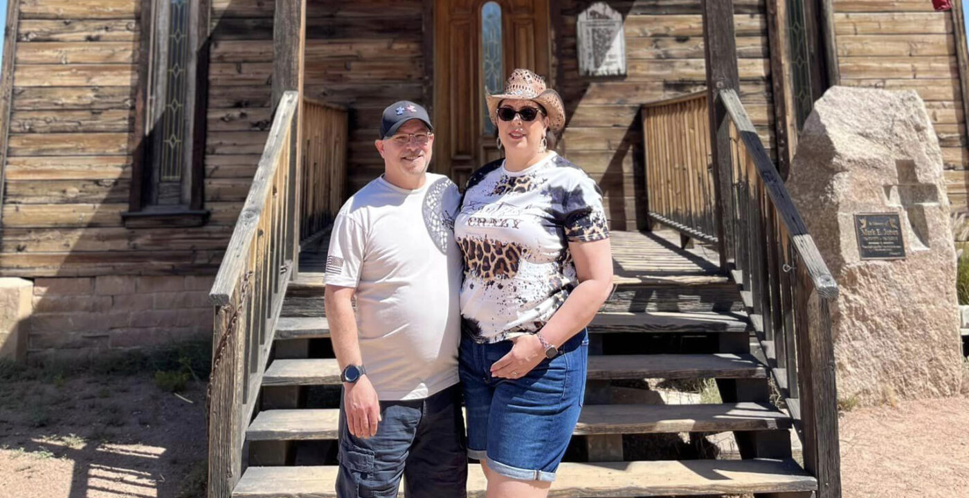Couple stands in front of a rustic building.