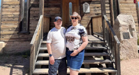 Couple stands in front of a rustic building.